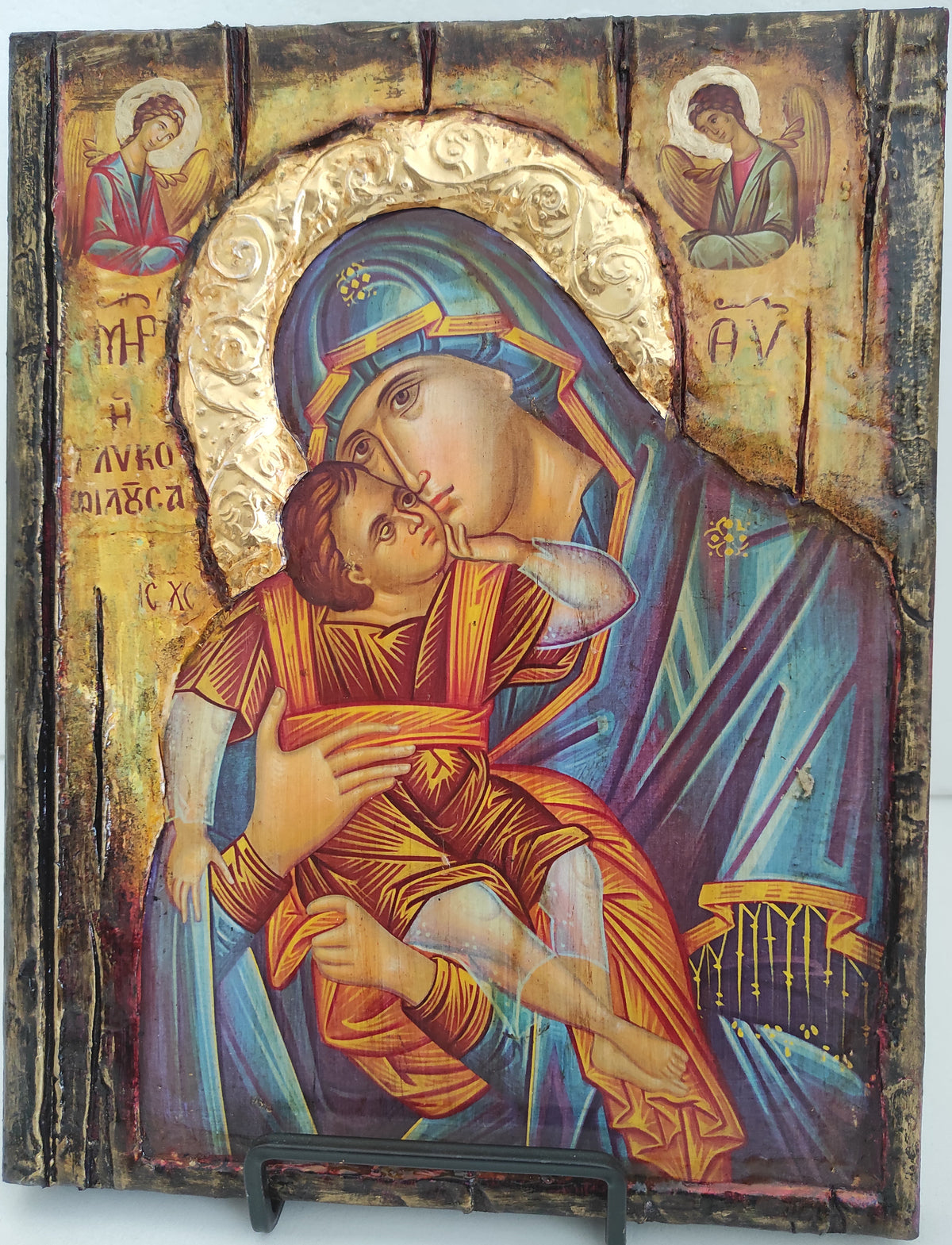 An antique wooden religious icon designing depicting the Holy Family, featuring a mother of God in a blue cloak and child in orange robes, mounted on a dark wooden panel with a metal hanger visible on the right.