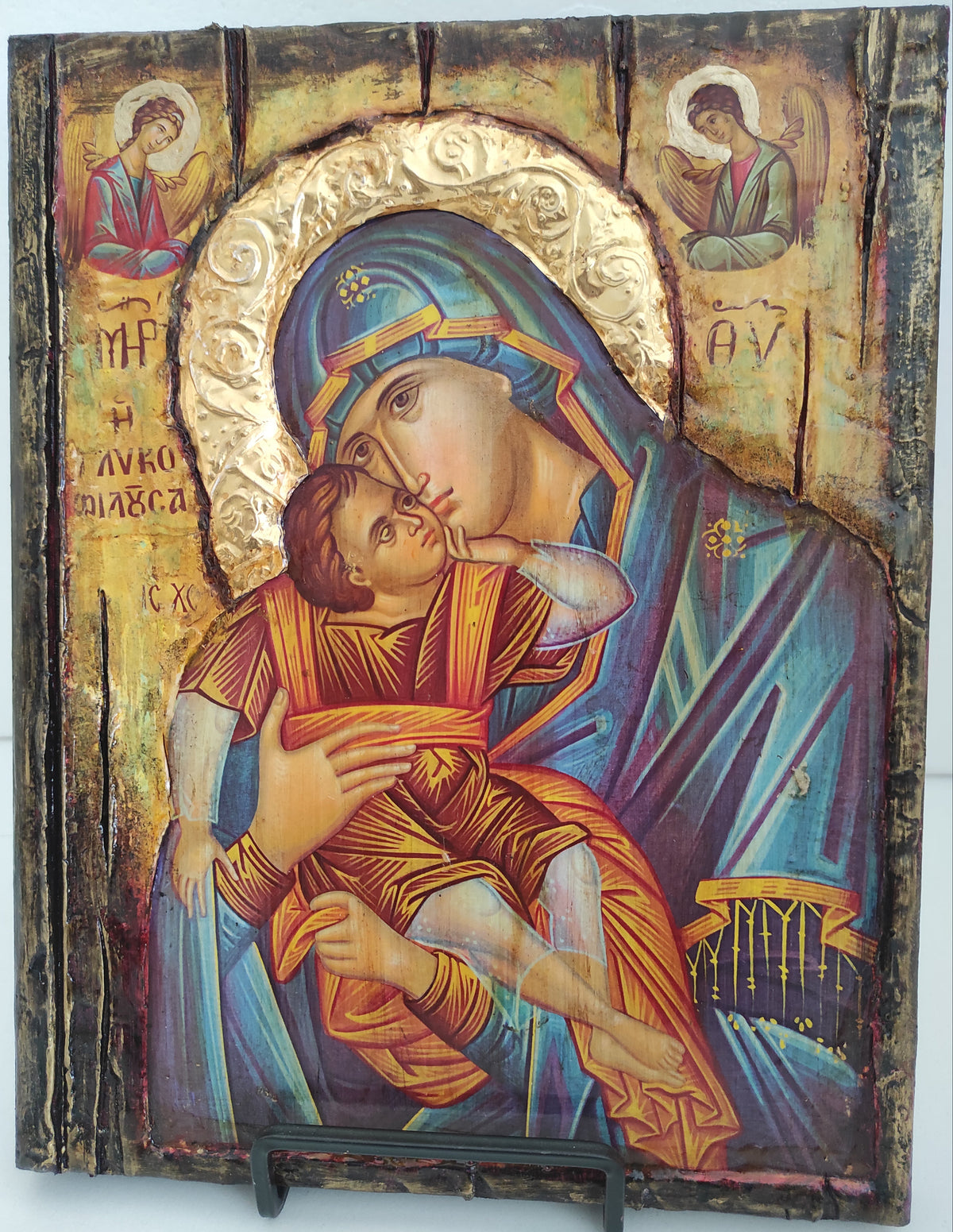 An antique wooden religious icon depicting the Holy Family, featuring a father figure in orange robes holding a child in a blue robe, with gold and brown painted details on a weathered wood panel.