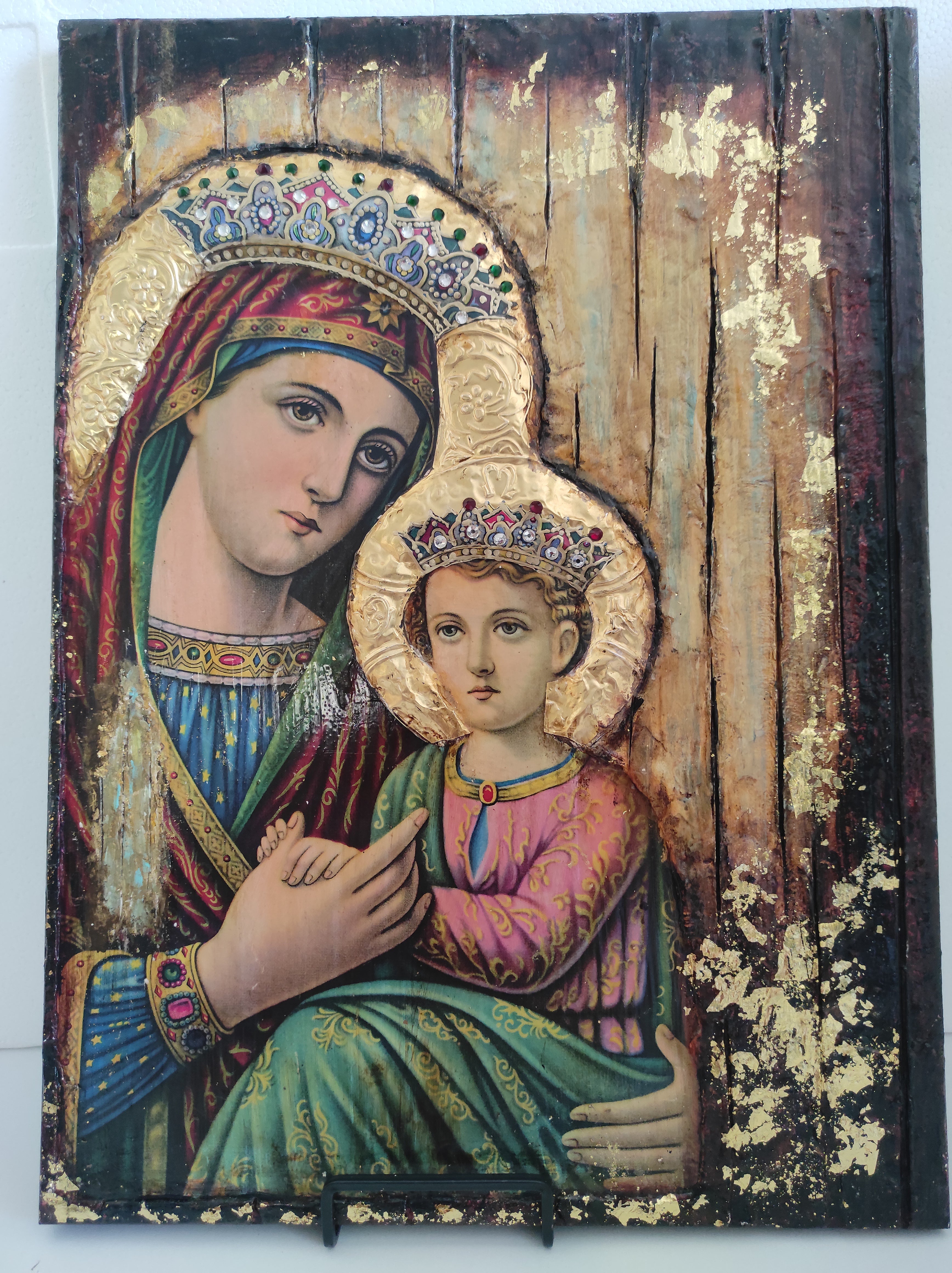 Decorative panel with religious icon of two figures, one holding a child, on a wooden background.
