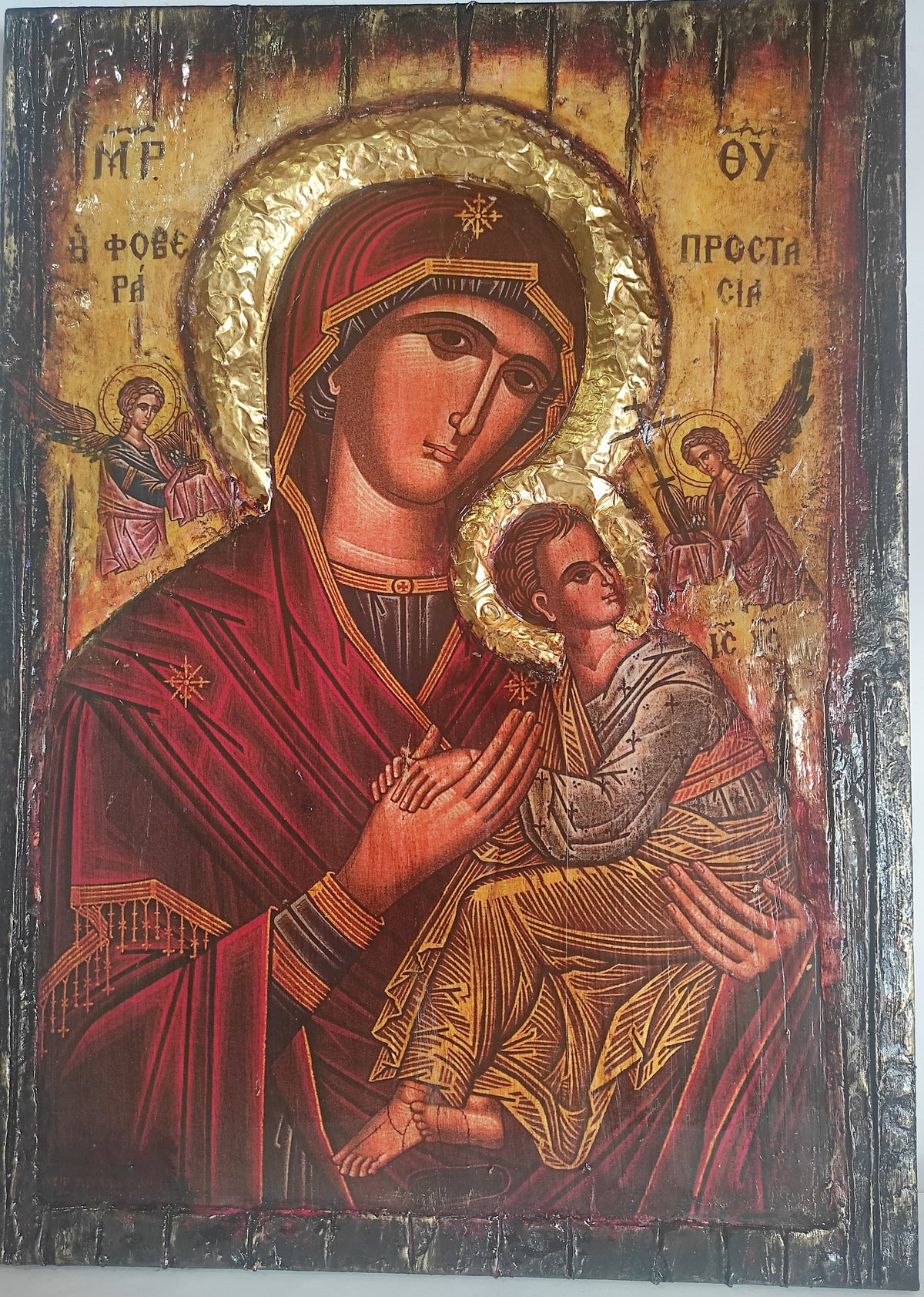 A Byzantine-style religious icon design of the Virgin Mary holding the infant Jesus, rendered in gold leaf and deep red tones with a dark wooden border.