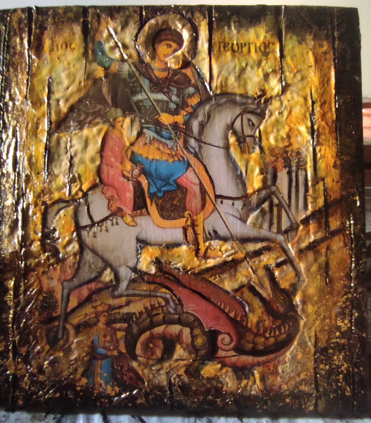 A Byzantine-style wooden icon design of Saint George on a white horse, featuring textured gold leaf, red drapery, and a dark brown background.
