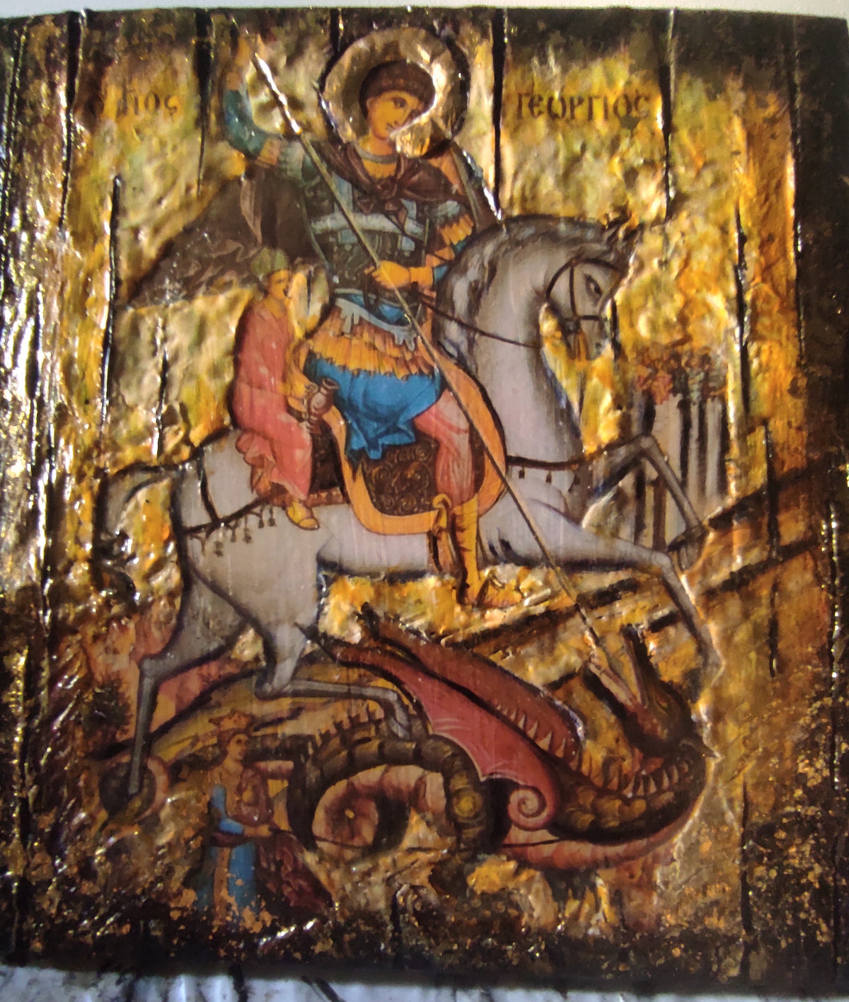 A Byzantine-style religious icon design on a wooden panel depicting Saint George on a white horse, with gold leaf texture and a dragon at the bottom.