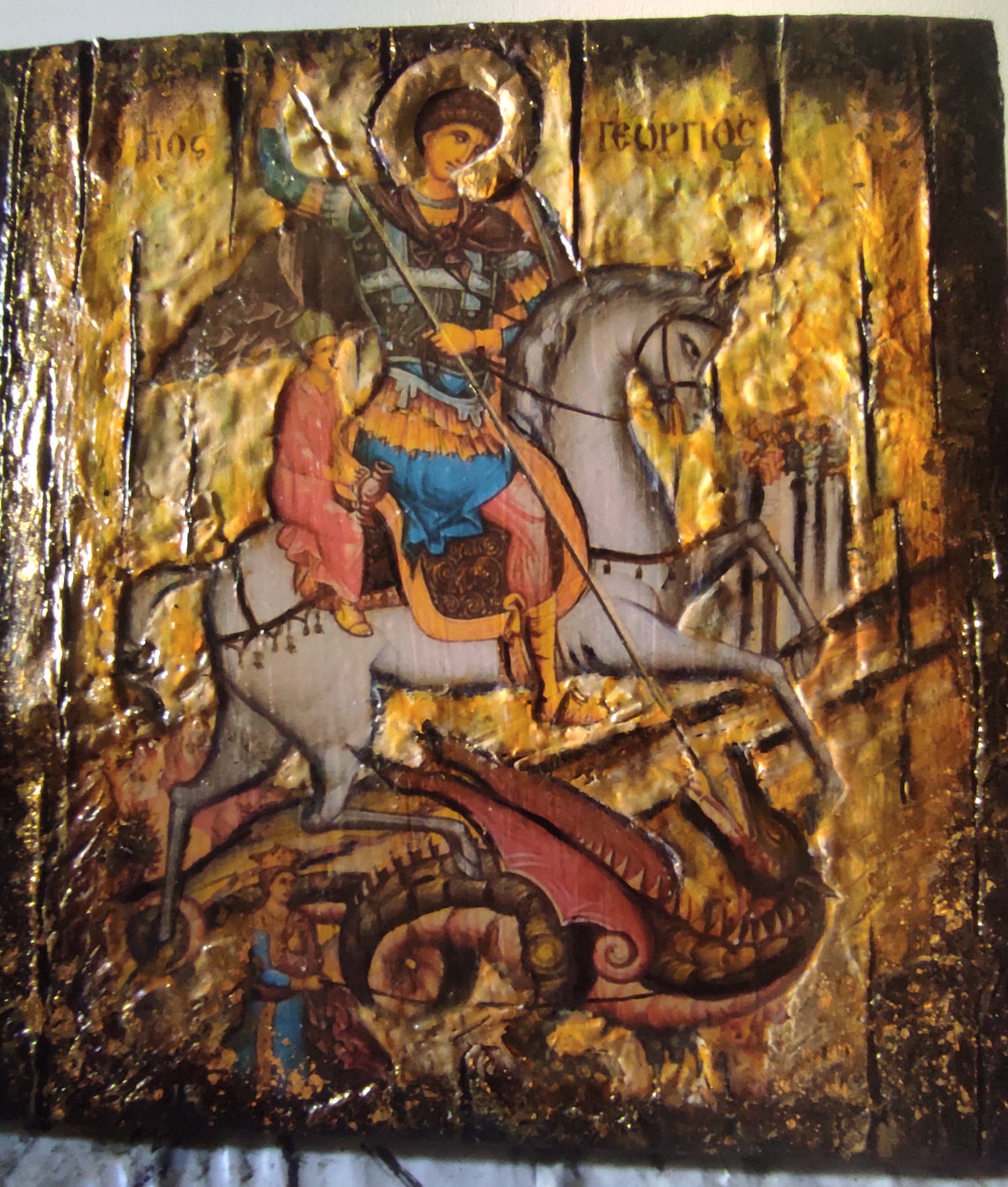 A Byzantine-style religious icon design on a gold leaf background, depicting Saint George on a white horse with a red dragon beneath him, with Cyrillic lettering at the top.