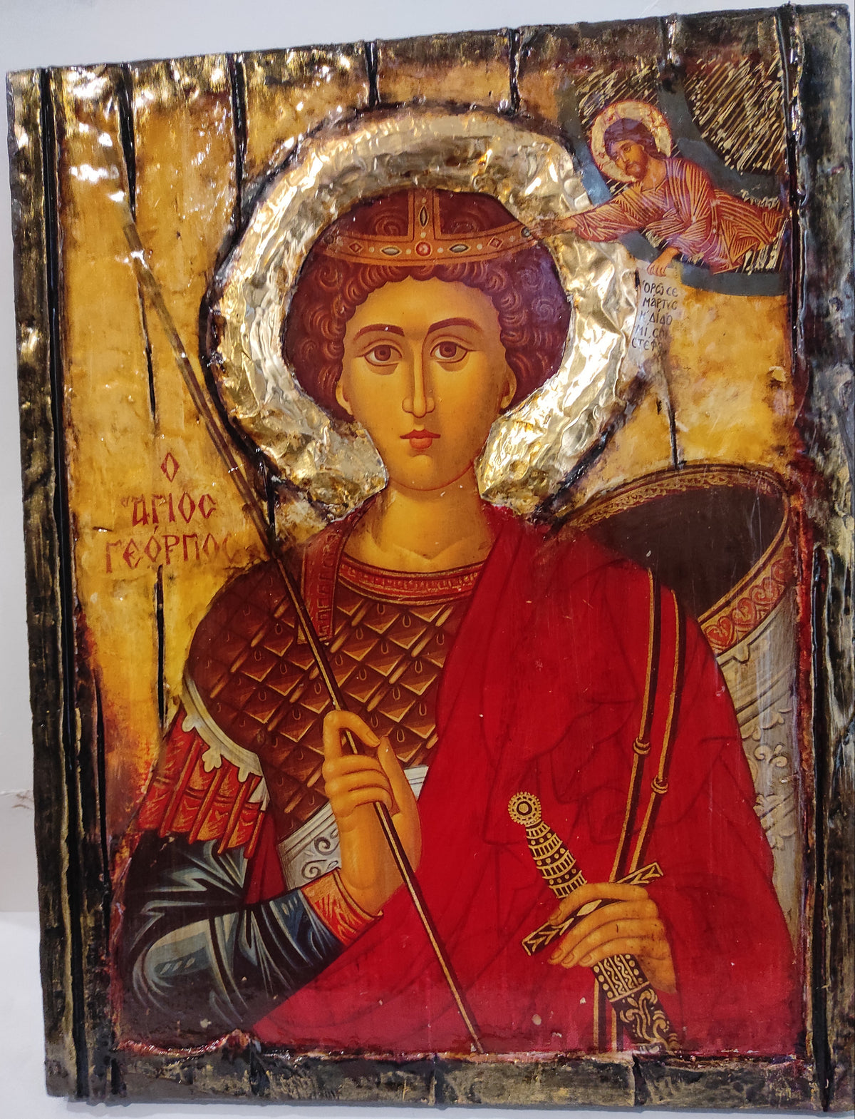 An antique religious icon design of Saint George on a wooden panel, featuring a gold background, a red robe, and a silver halo.