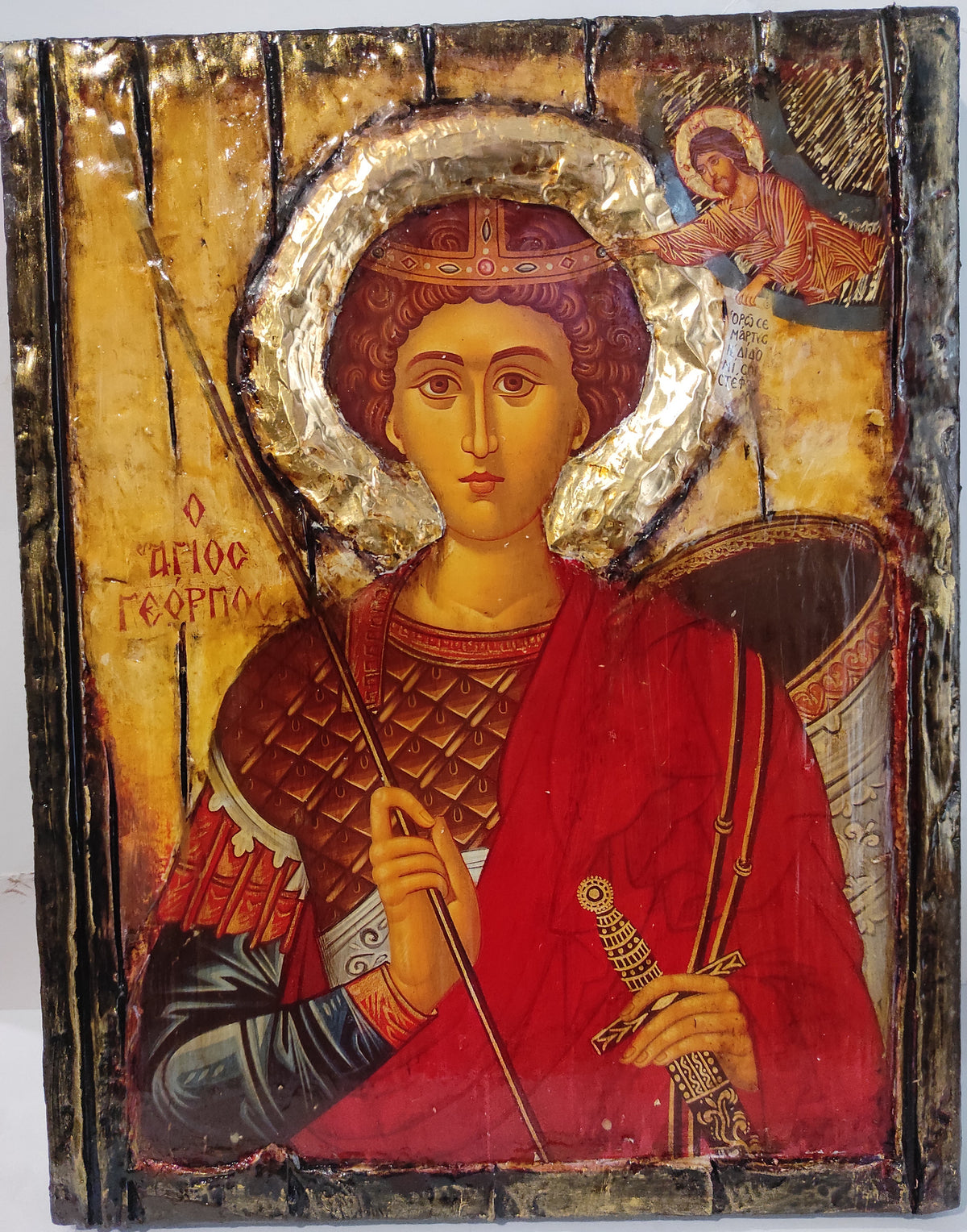 An antique religious icon design of Saint George on a wooden panel, featuring a red robe, gold halos, and a winged angel in the upper right corner.