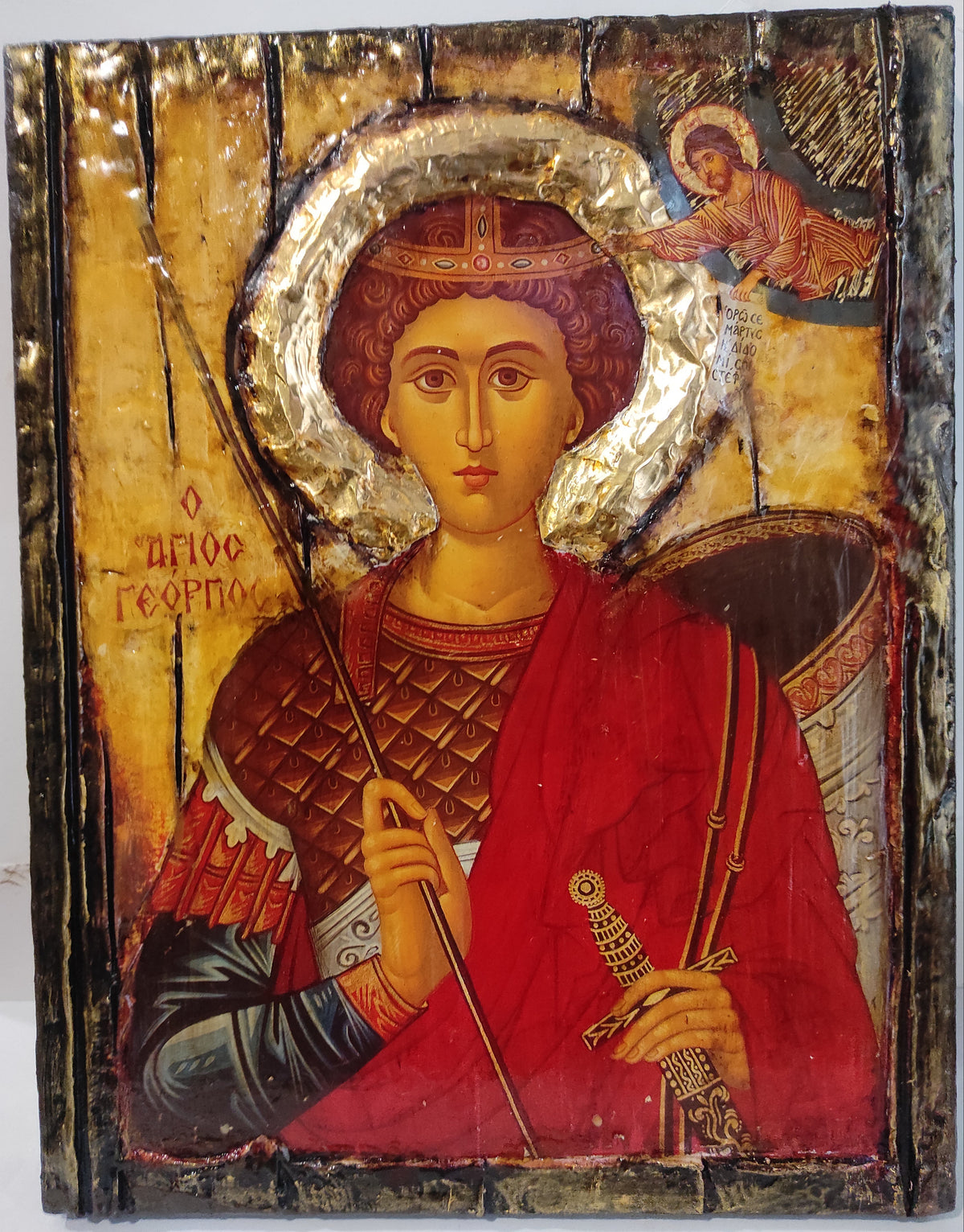 An antique wooden Byzantine-style religious icon of Saint George on a gold background, featuring a red robe, armor, and a silver gilded halo.