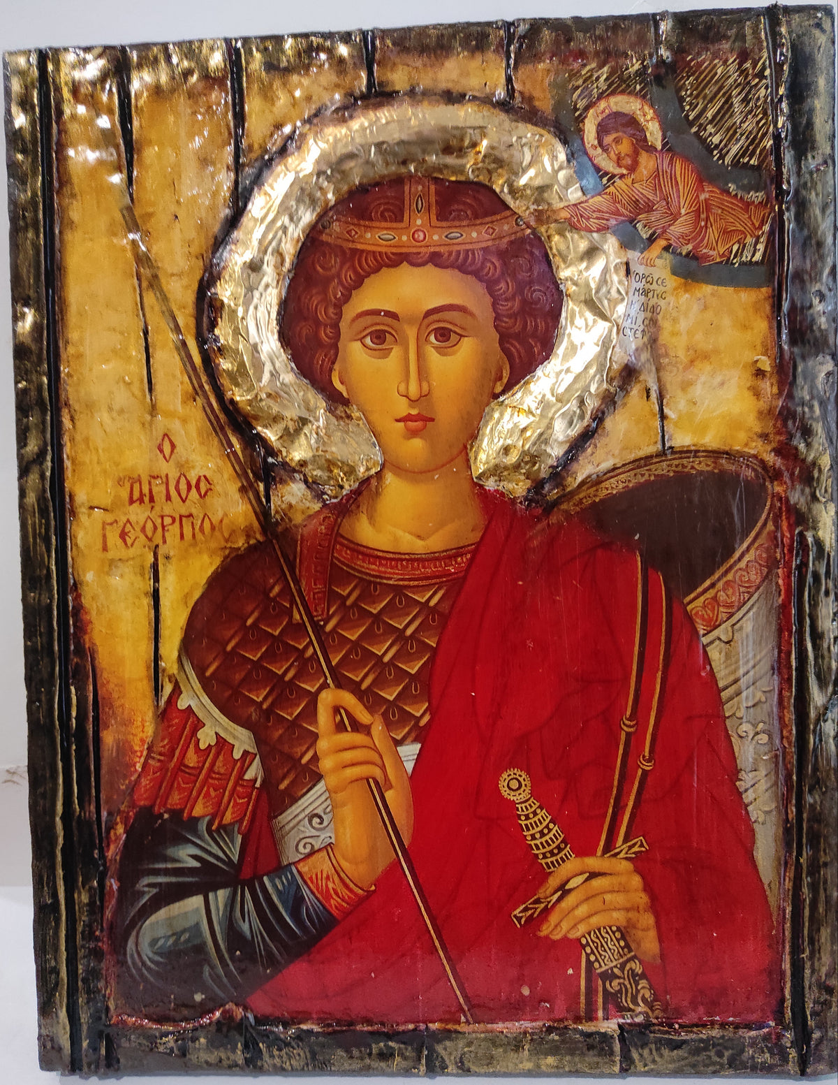 An antique wooden religious icon design of Saint George, featuring a gold leaf background, a red robe, and a silver halo, photographed against a plain white background.
