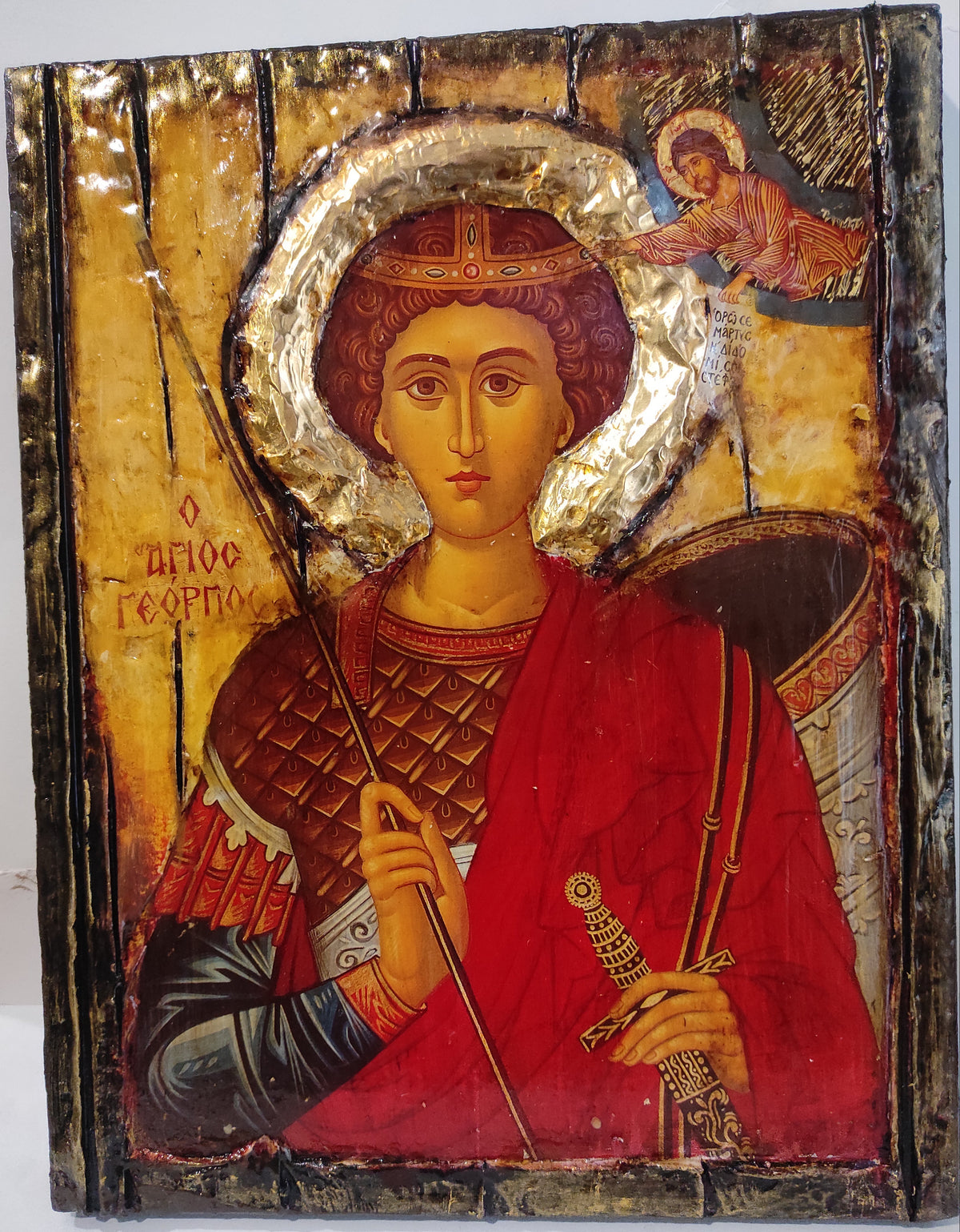 An antique wooden Orthodox icon of Saint George holding a sword and spear, featuring a gold leaf halo and red robe on a distressed wooden panel.
