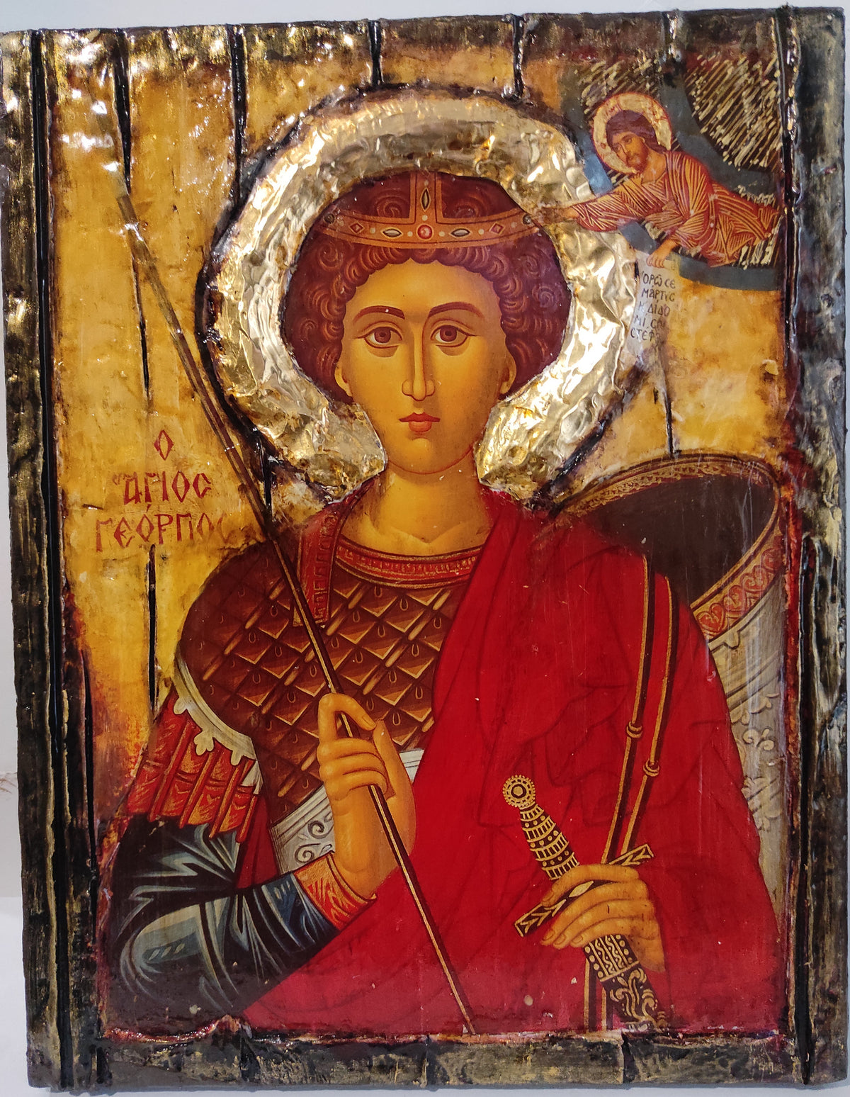 An antique wooden religious icon design of Saint George, featuring a gold background, a red robe, and a silver halo, with a small angel in the upper right corner.