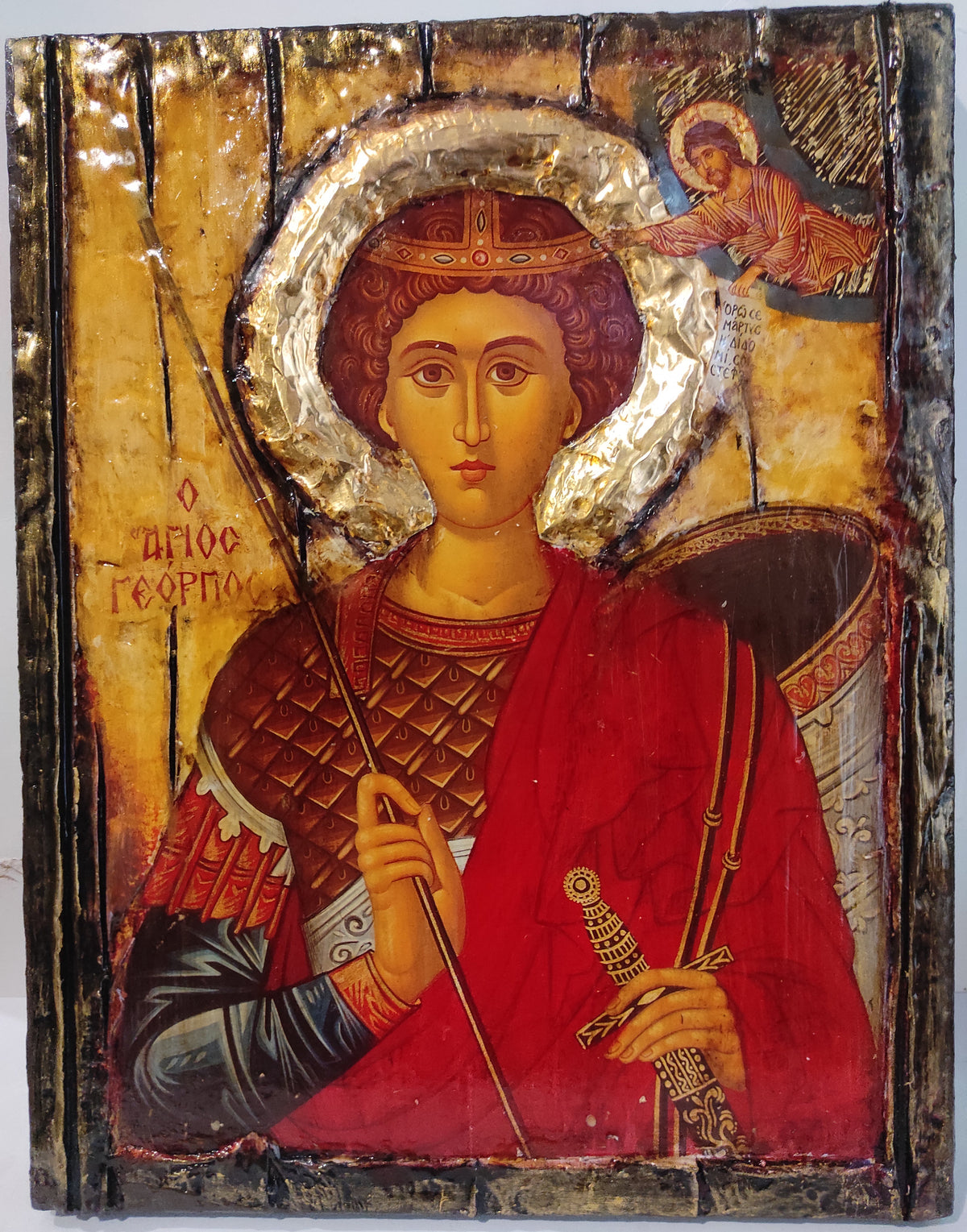 An antique wooden religious icon design of Saint George, featuring a gold background, a red robe, and a silver-gilded halo, with a small angel in the upper right corner.
