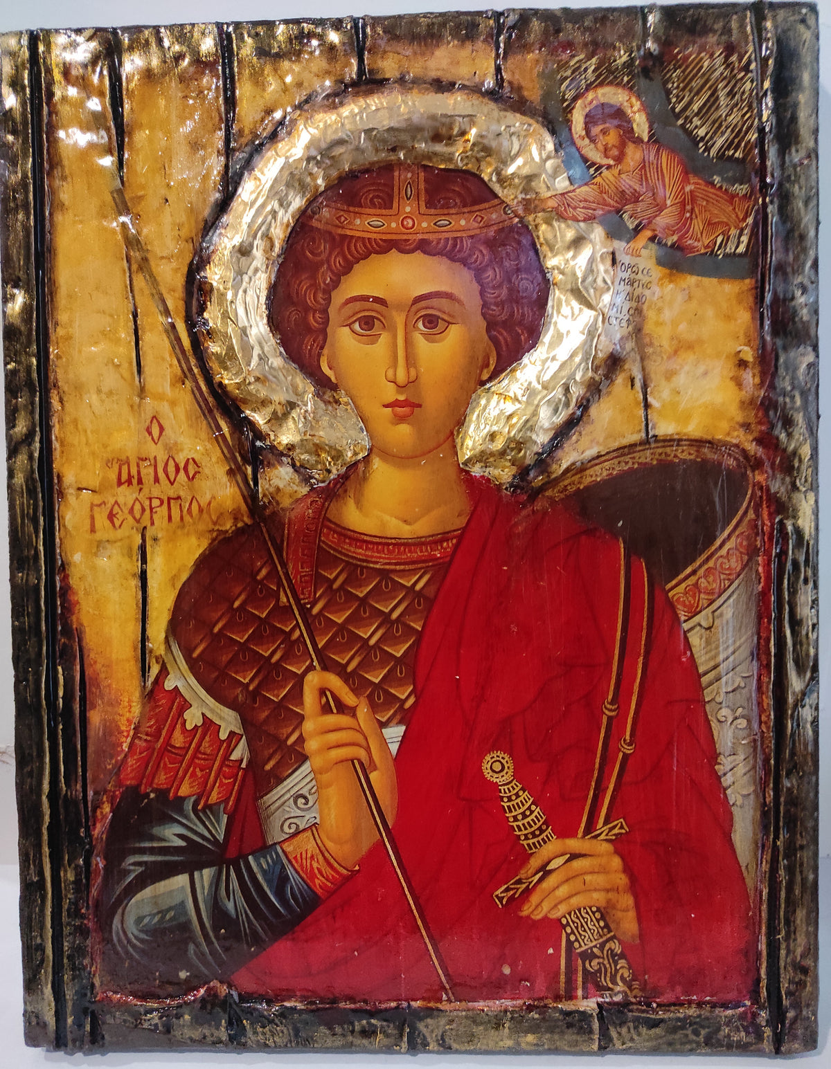 An antique wooden religious icon of Saint George on a gold background, featuring a red robe, a silver halo, and a small angel in the upper right corner.