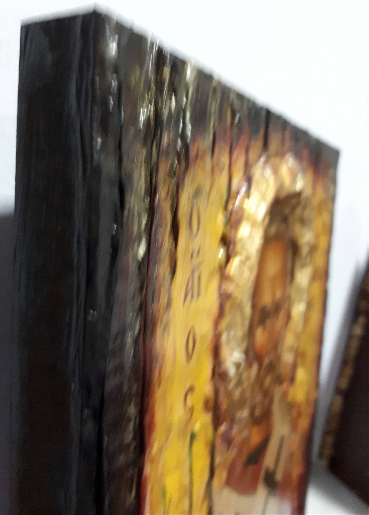 A close-up of a wooden plaque or icon with a gold-toned religious portrait and vertical text, photographed against a plain light background.