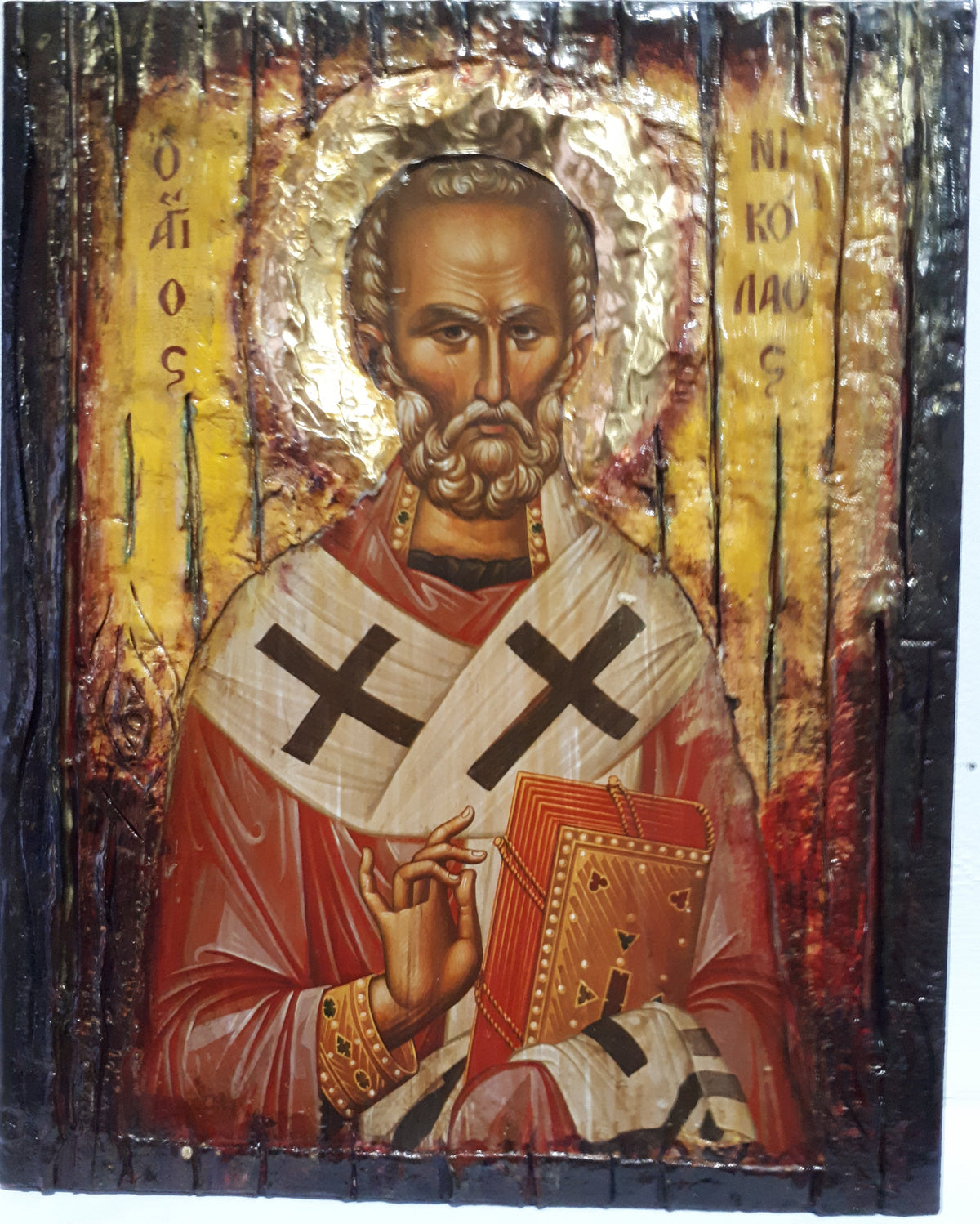 A rustic wooden religious icon design of Saint Nicholas, featuring a textured gold background, red and white robes with black crosses, and a dark charred wood border.