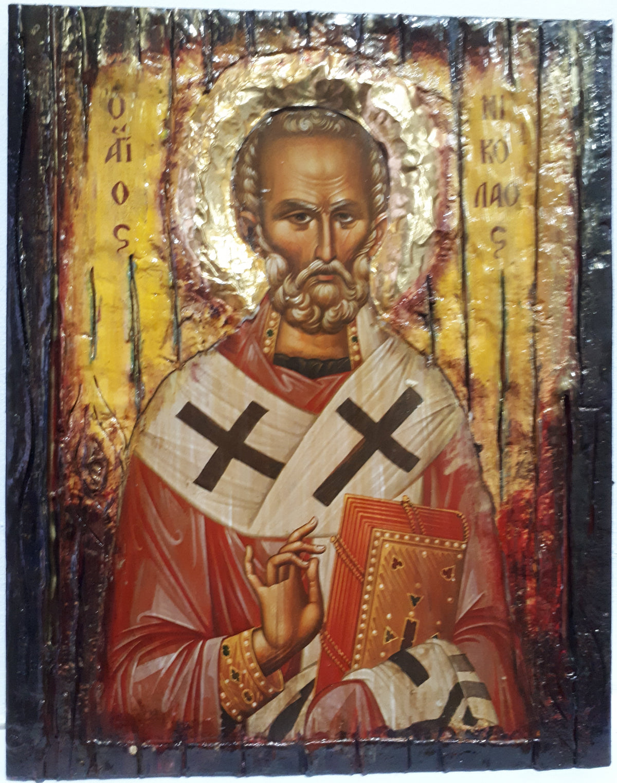 A religious icon design of Saint Nikolas on a dark wooden panel, featuring gold leaf detailing, a red robe, and a white episcopal cloak with black crosses.