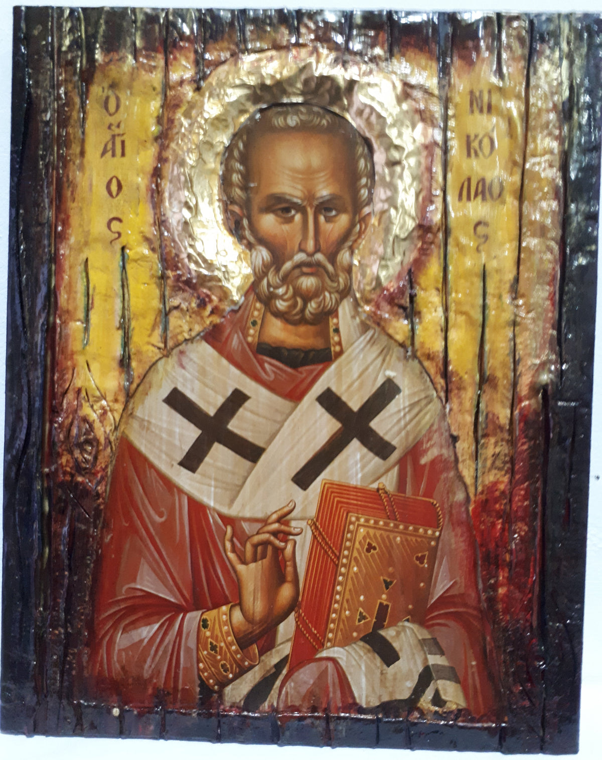 A rustic wooden religious icon design of Saint Nicholas, featuring a gold halo, red and white robes with black crosses, and Greek lettering on a distressed wood background.