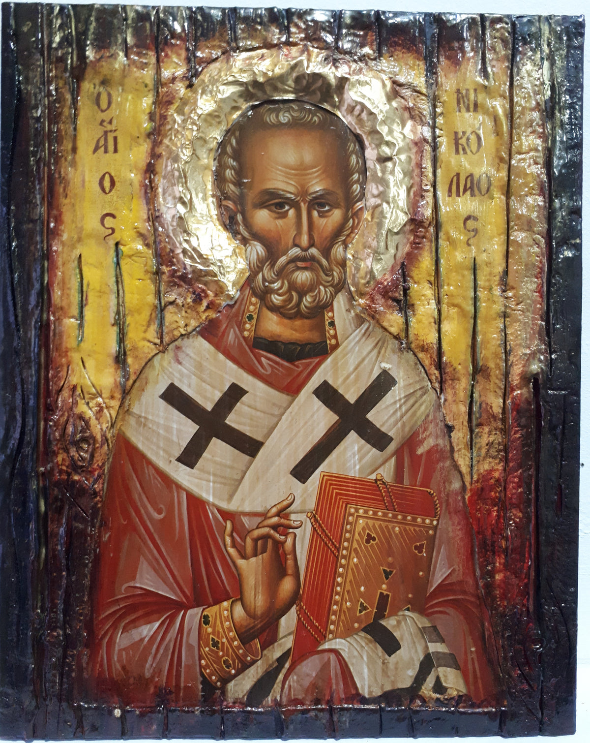 A Byzantine-style religious icon design on a dark wooden panel, depicting Saint Nicholas wearing a red robe and white episcopat veil with black crosses, holding a book, against a gold background with Greek lettering.