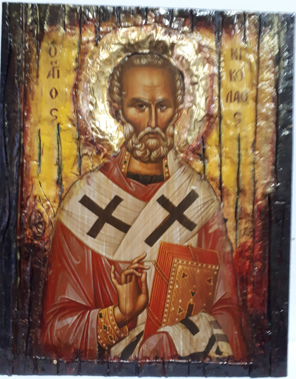 A rustic wooden religious icon design of Saint Nikolas, featuring gold leaf halos, red and white robes, and a textured dark wood border.