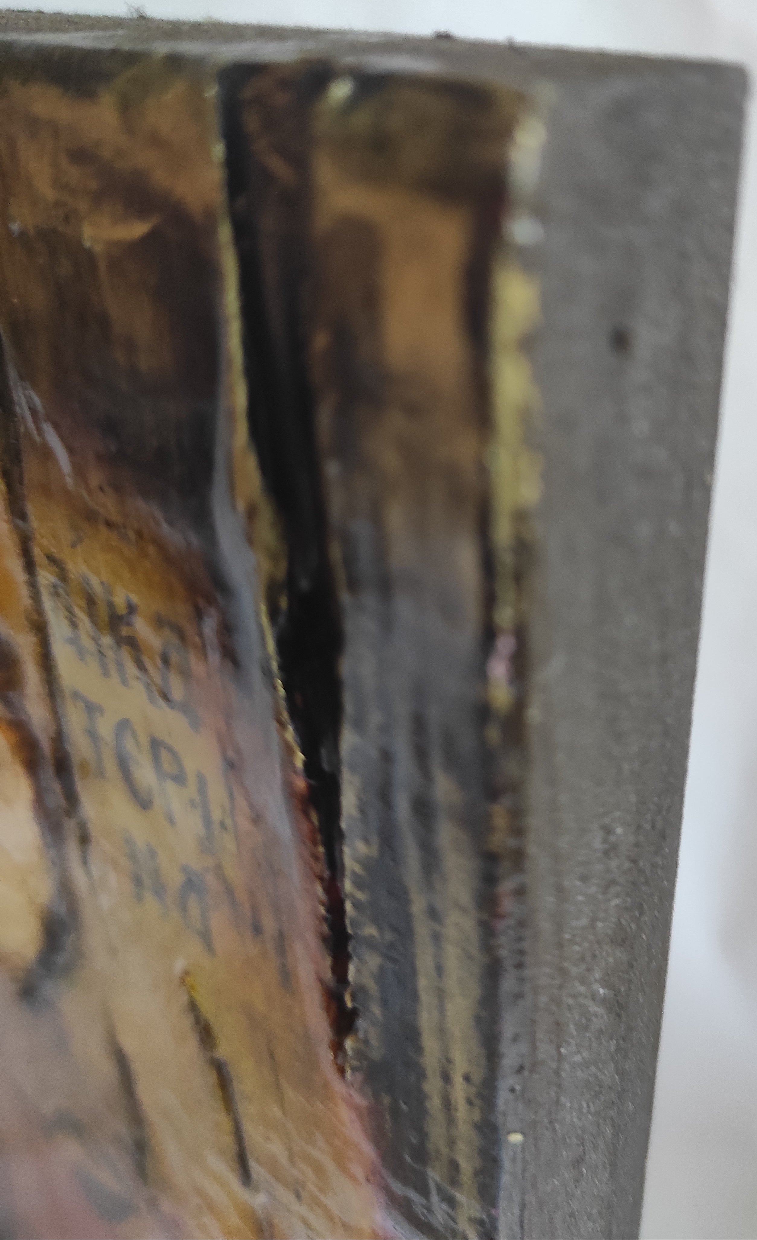 Close-up of a textured wooden surface with dark brown, black, and golden-brown painted details, showing a rough, weathered finish against a white background.
