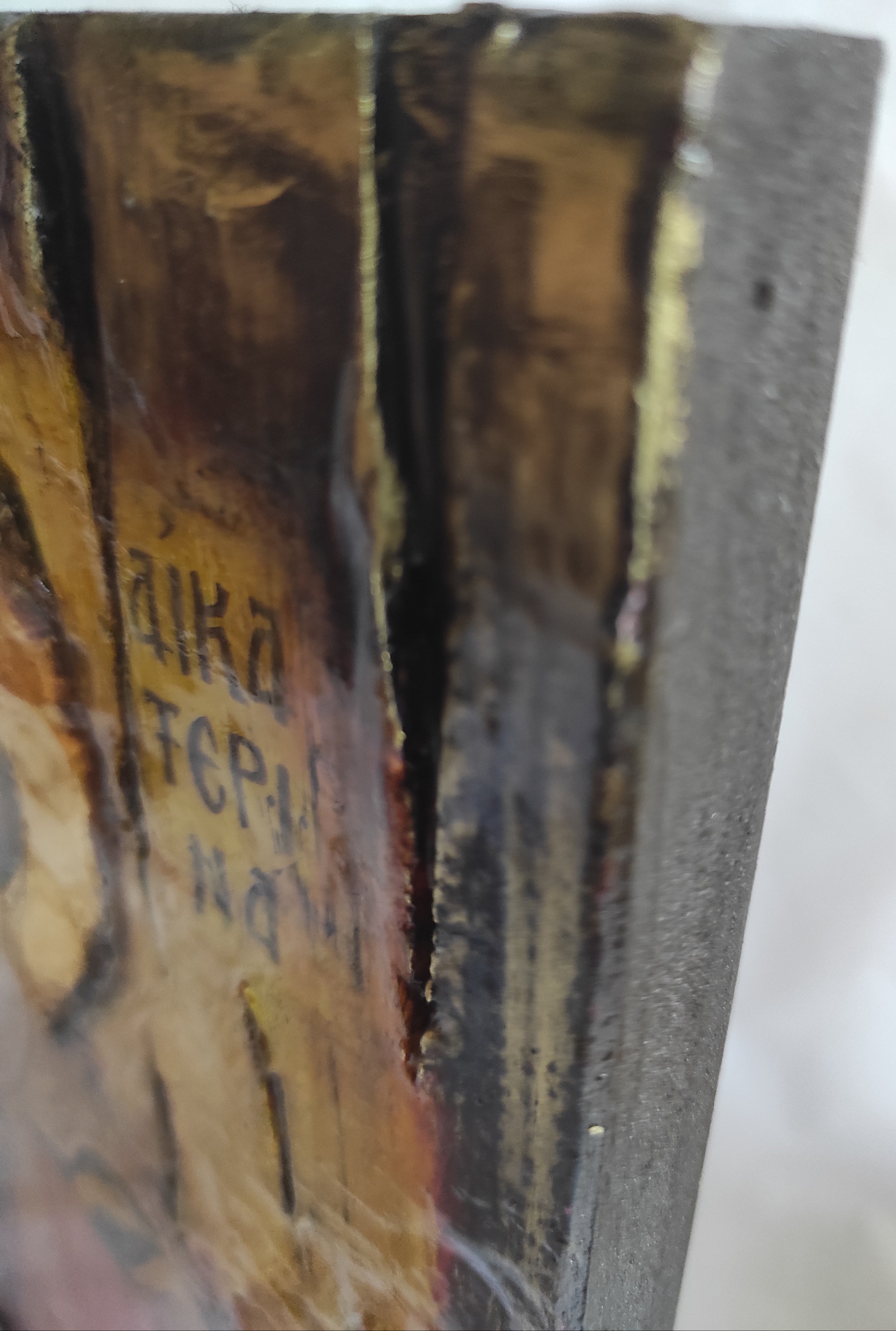 Close-up of a textured wooden block or panel with dark gray on top, layered golden-brown wood beneath, and Cyrillic lettering printed in dark ink.