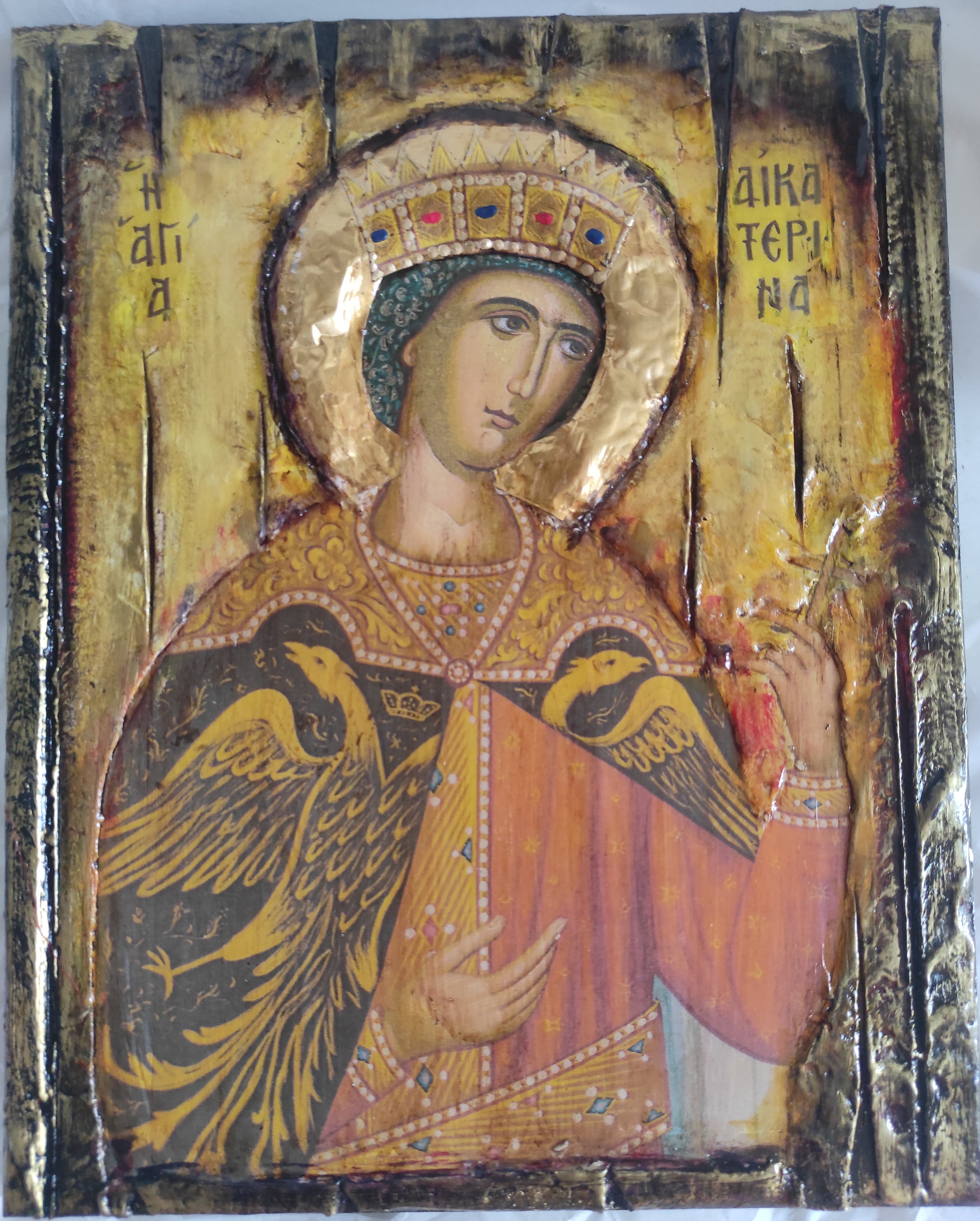 An Eastern Orthodox religious icon of St Ekaterinai, featuring gold leaf, a painted face, and a large eagle, photographed on a white background.