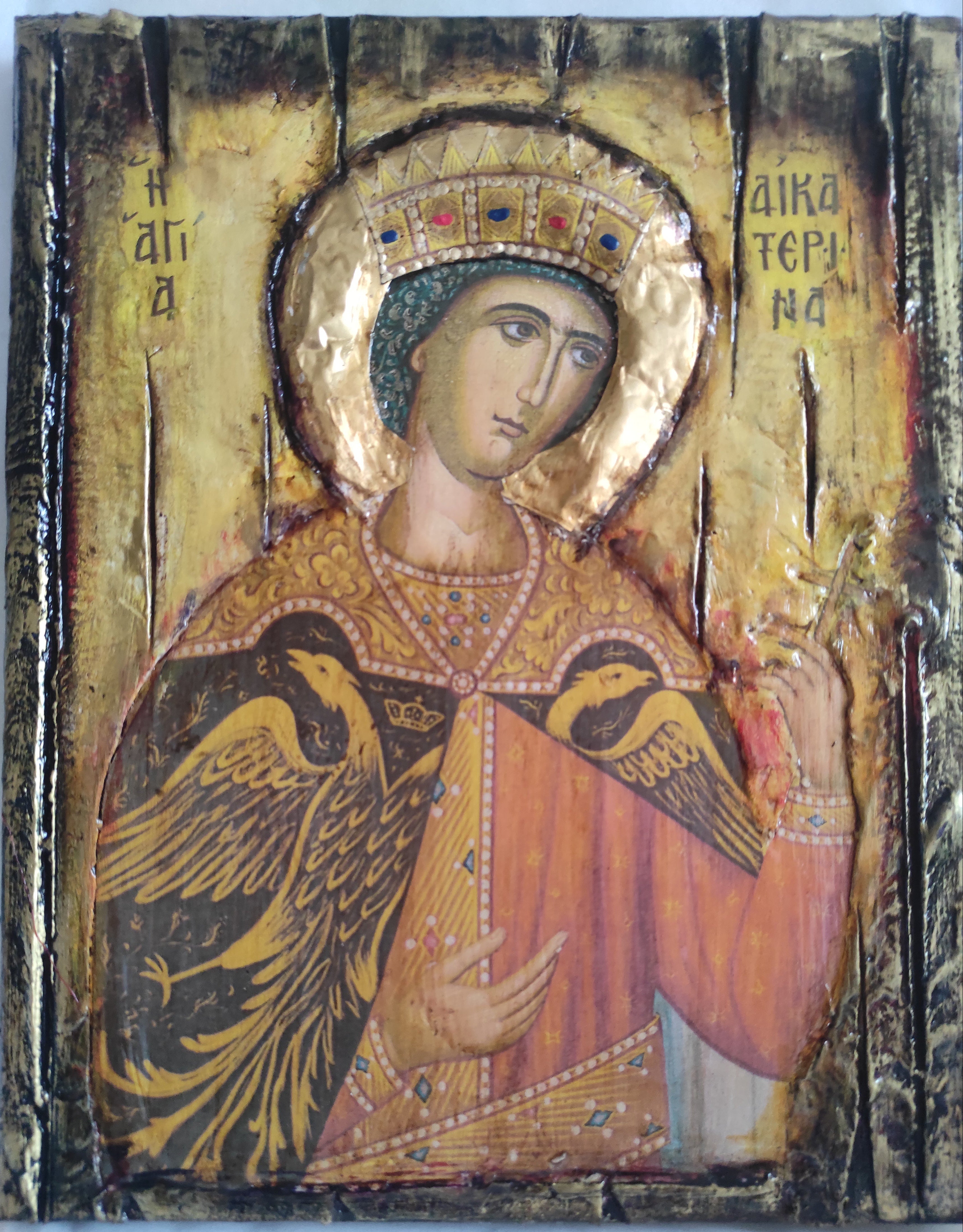An antique Byzantine-style religious icon painting on a wooden panel, depicting a saint with a gold halo and a red robe, with two black birds on the chest, set against a plain light background.