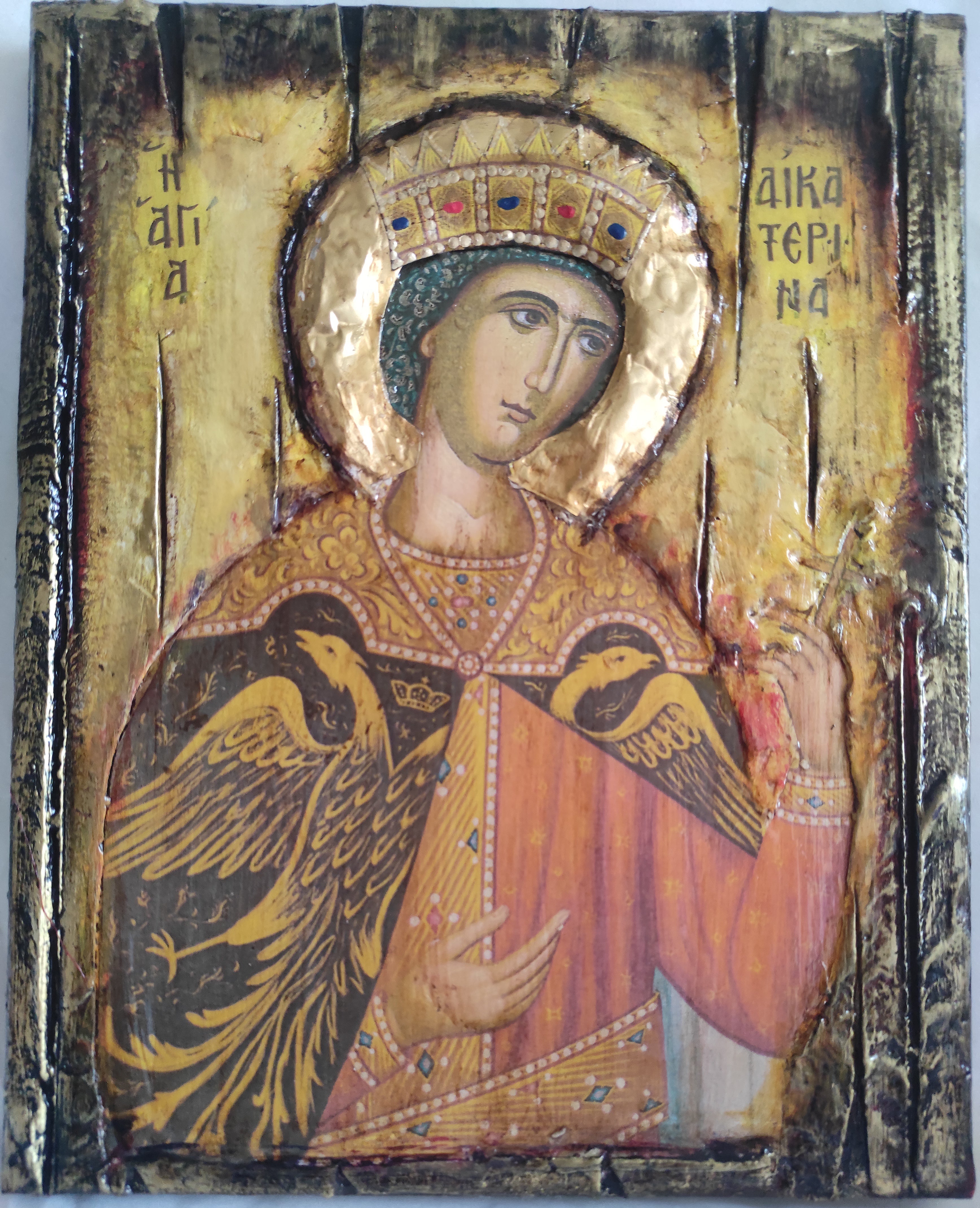 An antique religious icon on a rustic wooden panel, depicting a saint with a gold halo and a black eagle, featuring a distressed, weathered finish.