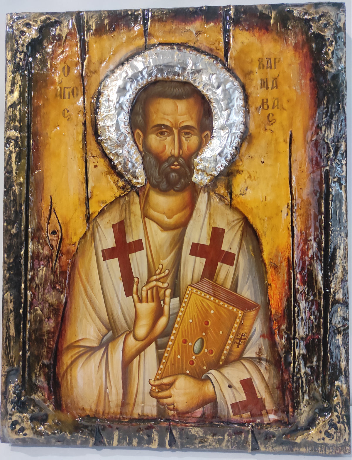 A traditional religious icon designof Saint Varnavas holding a book, featuring a gold background, silver foil halo, and distressed black borders.