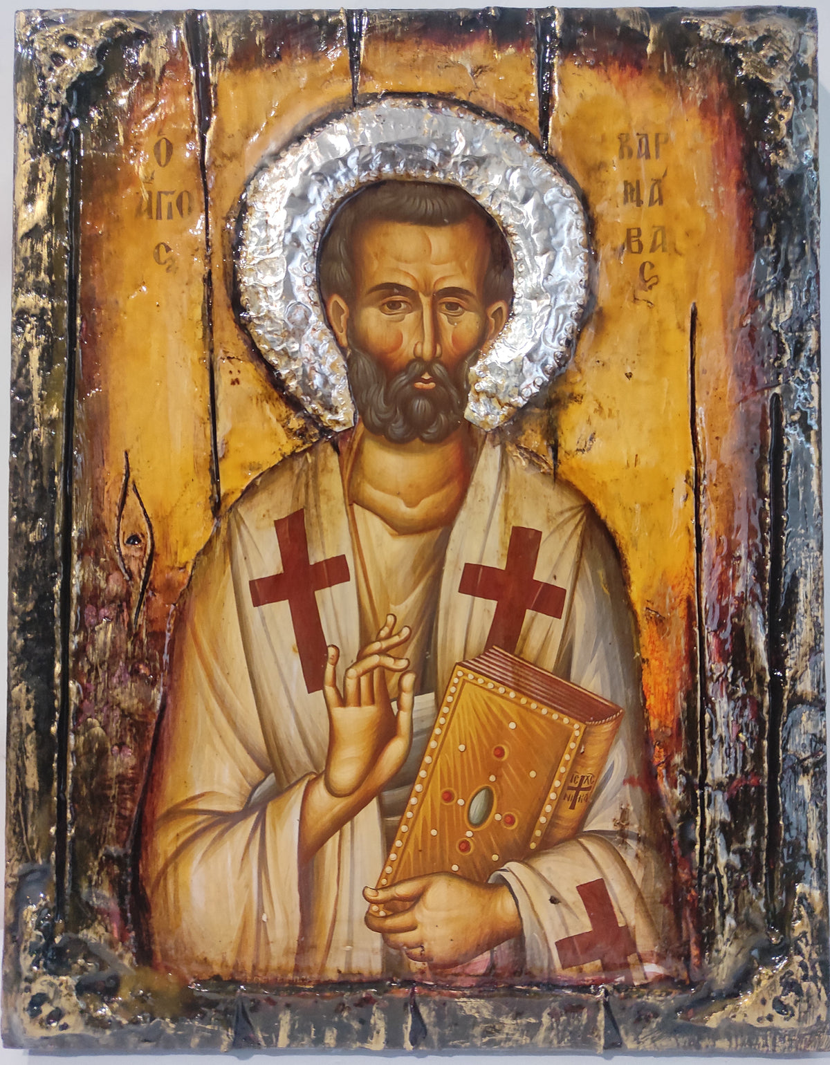 An antique-style religious icon design of Saint Barnabas on a wooden panel, featuring a gold background, silver foil halo, and red crosses on his garments.