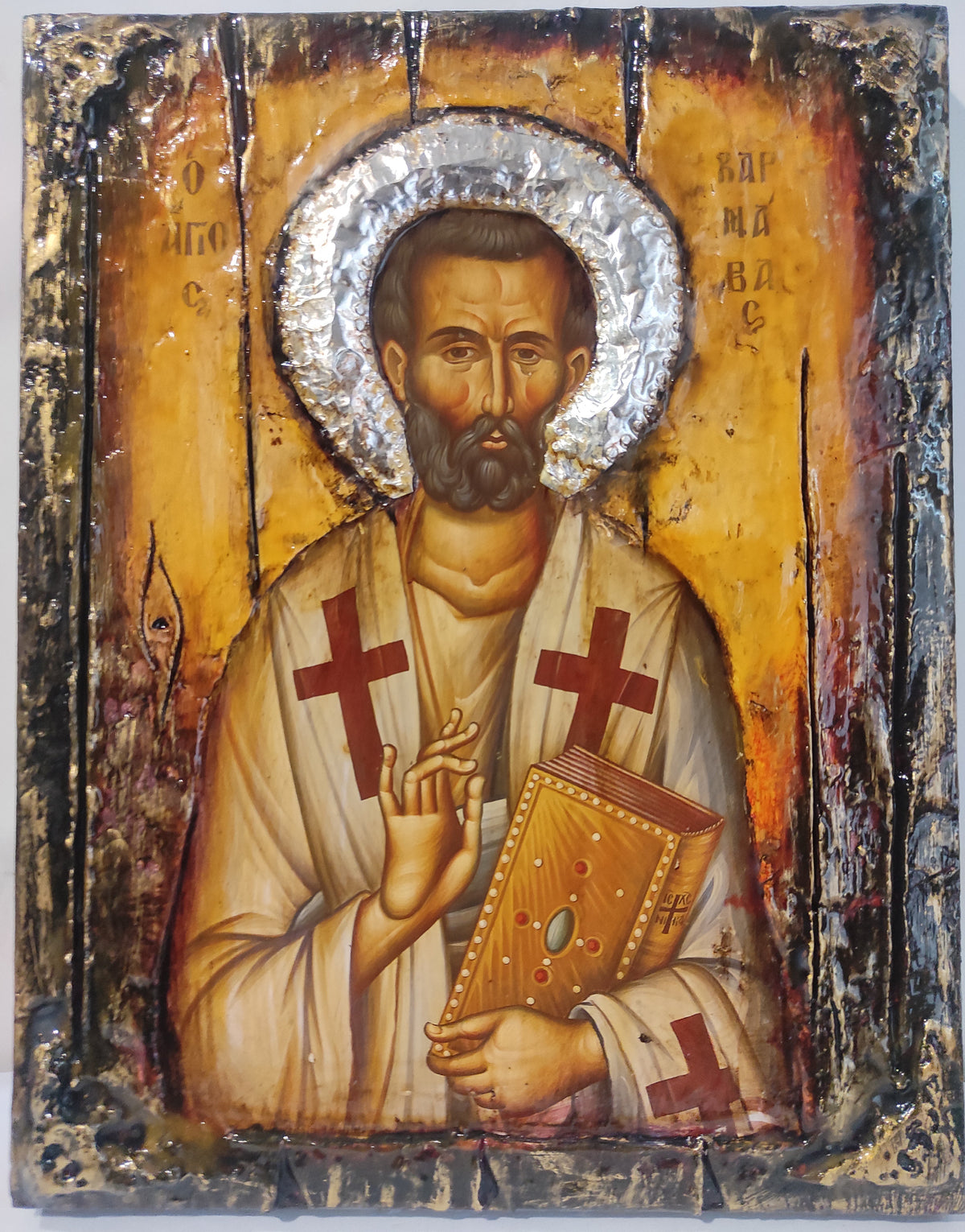 A religious icon design of Saint Barnabas holding a book, featuring a gold background, silver foil halo, and distressed black and brown borders.