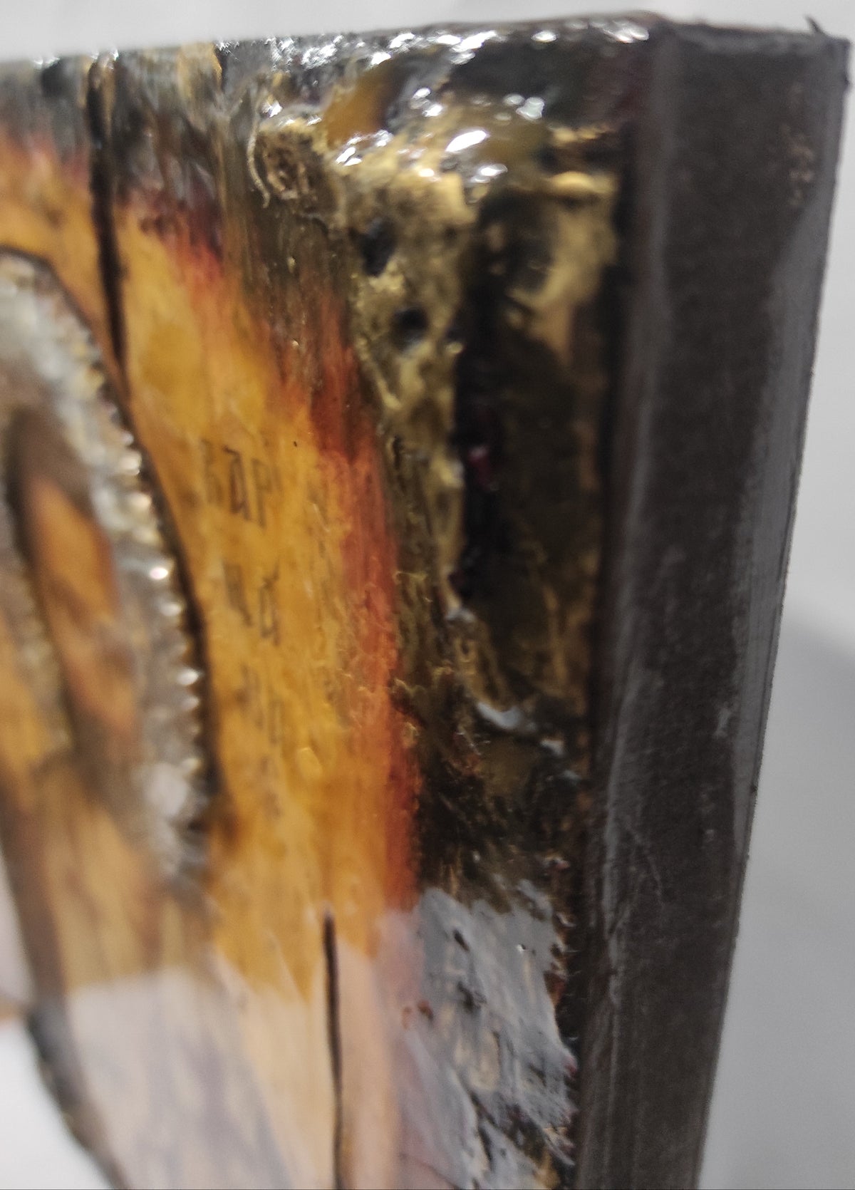 Close-up of a textured abstract artwork showing glossy black, gold, and orange-brown tones with a dark side edge on a light background.