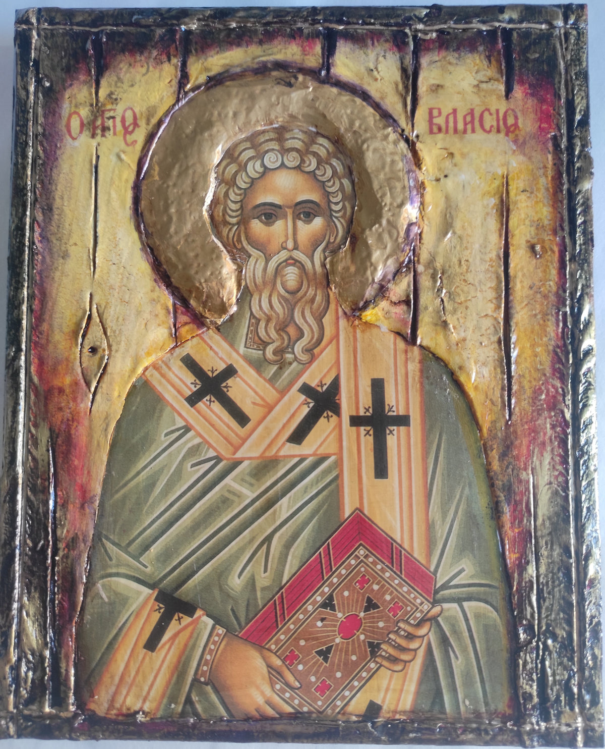 An antique-style religious icon design of Saint Vlasis, featuring a gold leaf halo, green and beige robes with black crosses, and red lettering on a distressed background.