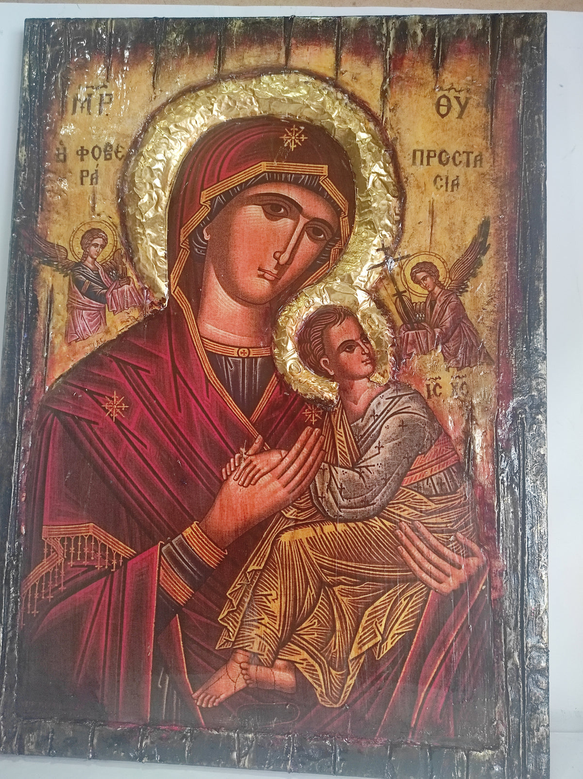 An antique-style religious icon design of the Virgin Mary holding the infant Jesus, with gold leaf-like halos and a dark wooden border around the artwork.